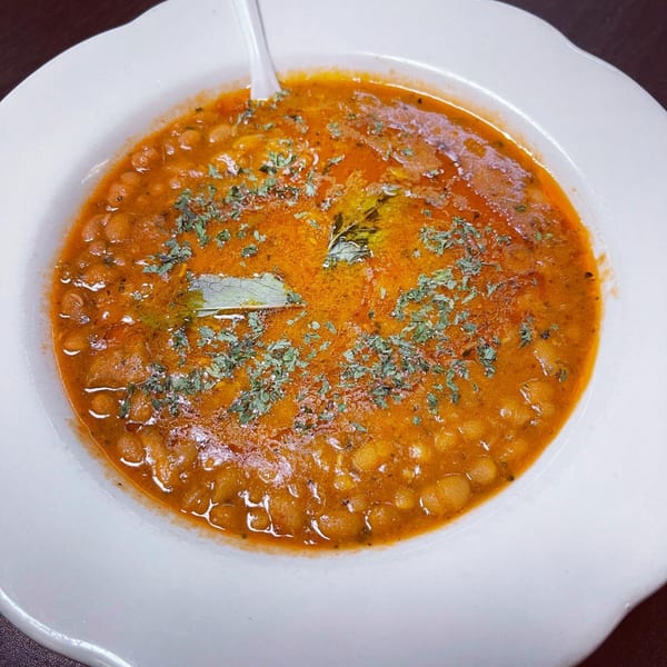 A white bowl filled with a rich, orange-red stew, garnished with fresh herbs.