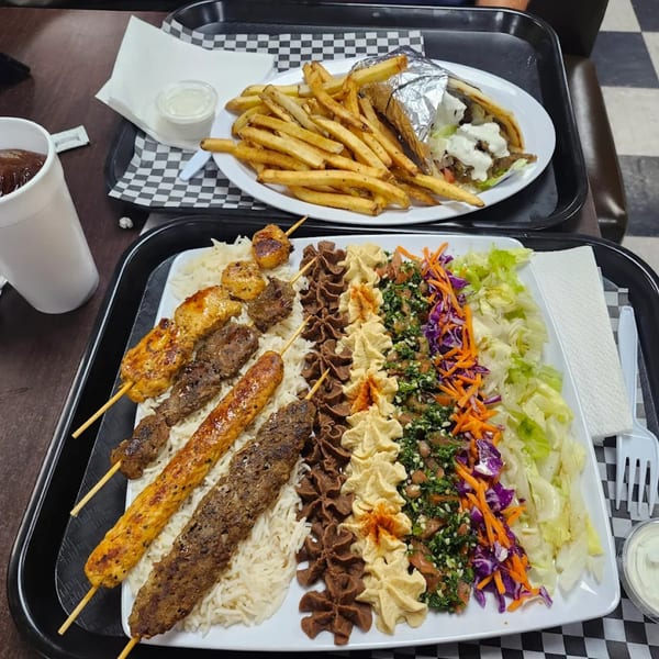 A large platter of Tikka Kabab's Mediterranean food with skewers, rice, hummus, salad, and a gyro.